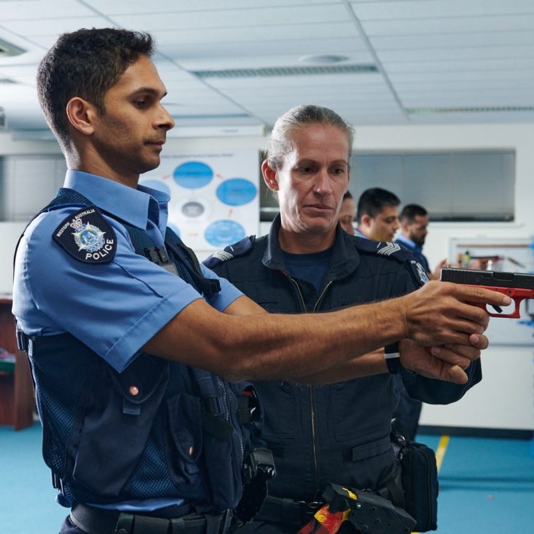 Police training officer assisting new recruit with firearms training.